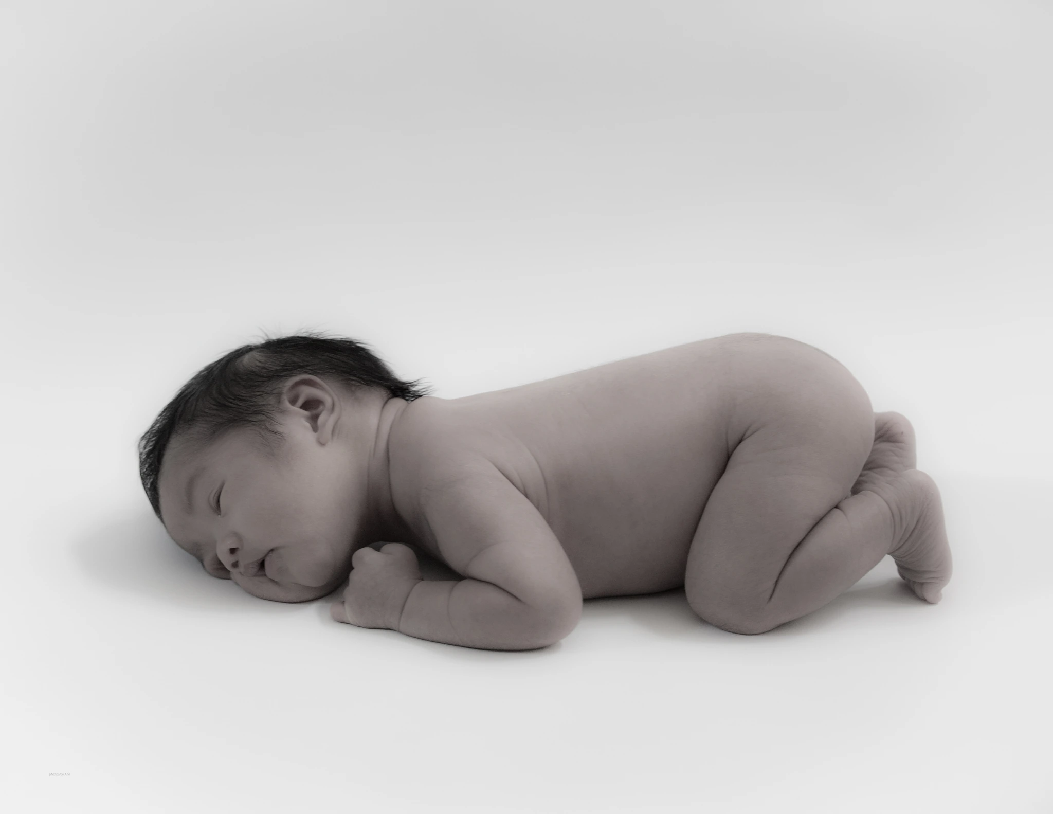 A sleeping newborn curled up on a plain white backdrop