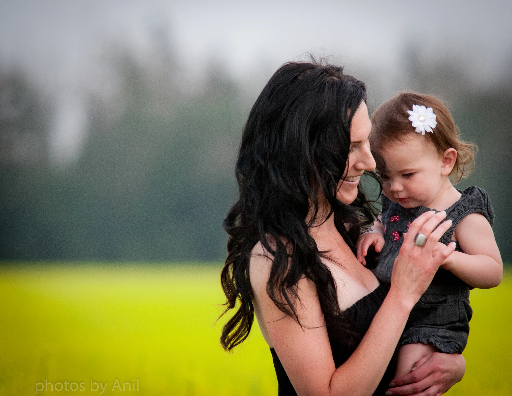 A mother holding her small daughter cheek to cheek at the edge of a blooming canola field
