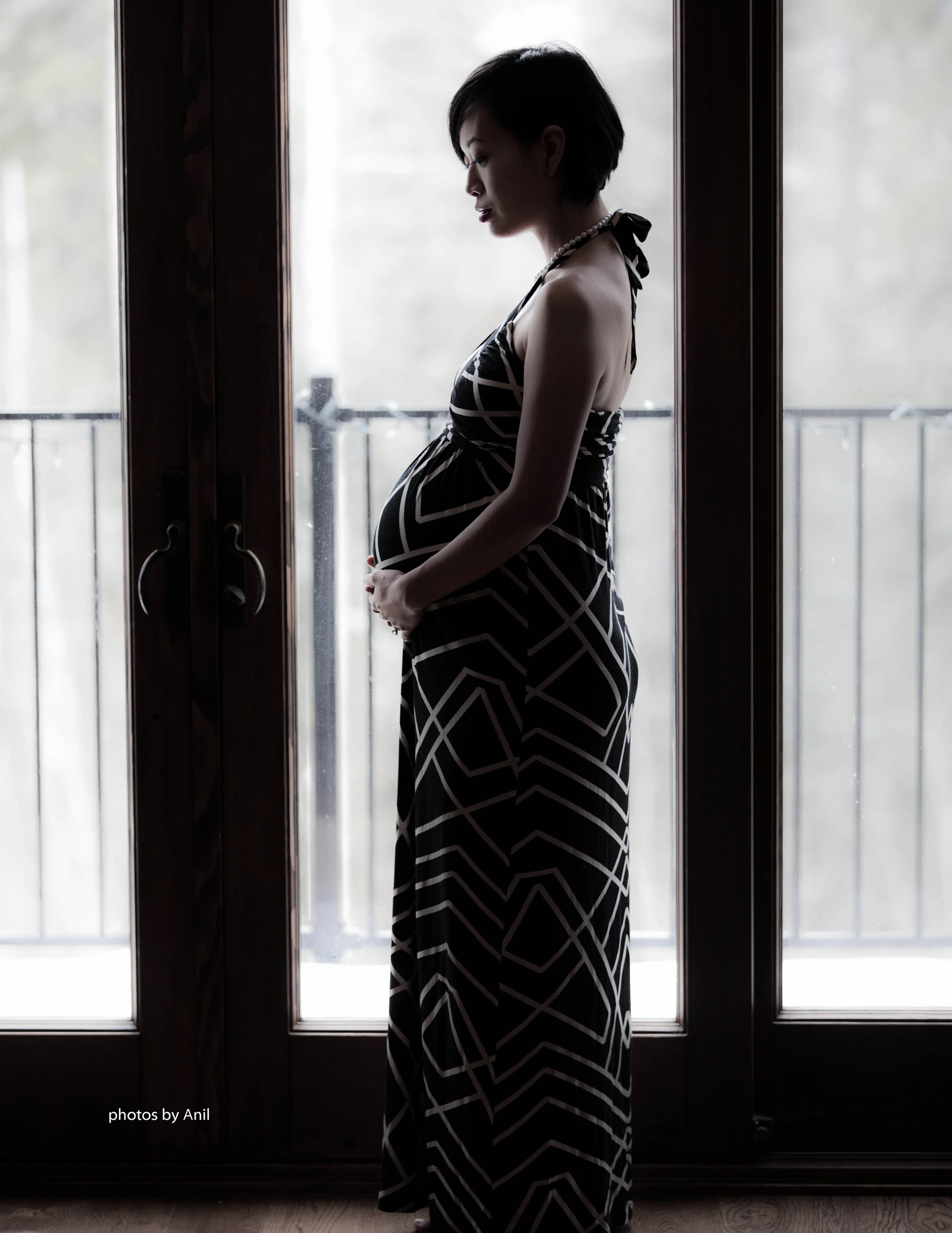 An expectant mother in profile against a tall bright window, hands resting on her bump